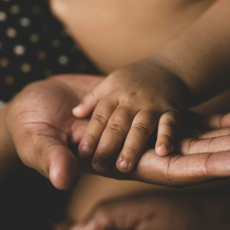 Telefon- und Onlineberatung Ein Erwachsener hält die kleine Hand eines Kindes in der eigenen Hand.