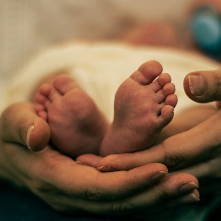 Stillvorbereitungskurse Zwei kleine Babyfüße, gehalten von einer erwachsenen Hand.