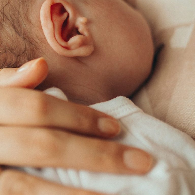 Persönliche Stillberatung Ein Erwachsener hält sanft einen Kopf eines schlafenden Babys.